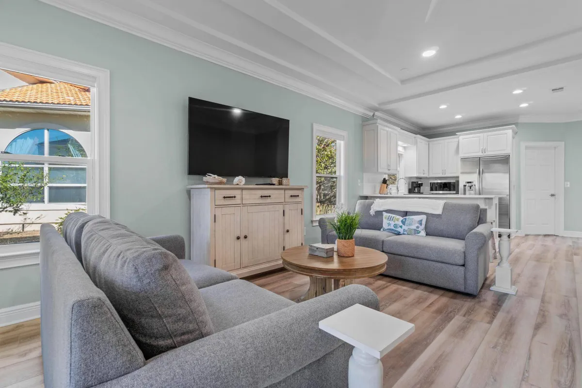 A bright, inviting living room featuring a comfortable sofa, a coffee table ideal for family board games or snacks, a TV for movie nights, and large windows that bring in plenty of natural light. The setup encourages relaxation and togetherness after a day spent exploring at the beach or pool.