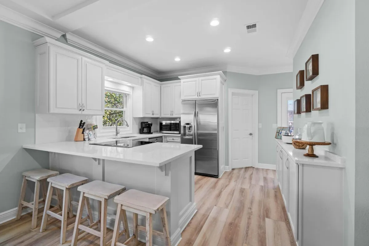 A kitchen island with white quartz countertops and bar stools, paired with a stainless steel refrigerator and white cabinetry. The island provides a casual spot for breakfast, snacks, or workspace, matching the description of a breakfast bar. The bright and clean space encourages both culinary creativity and casual interaction.
